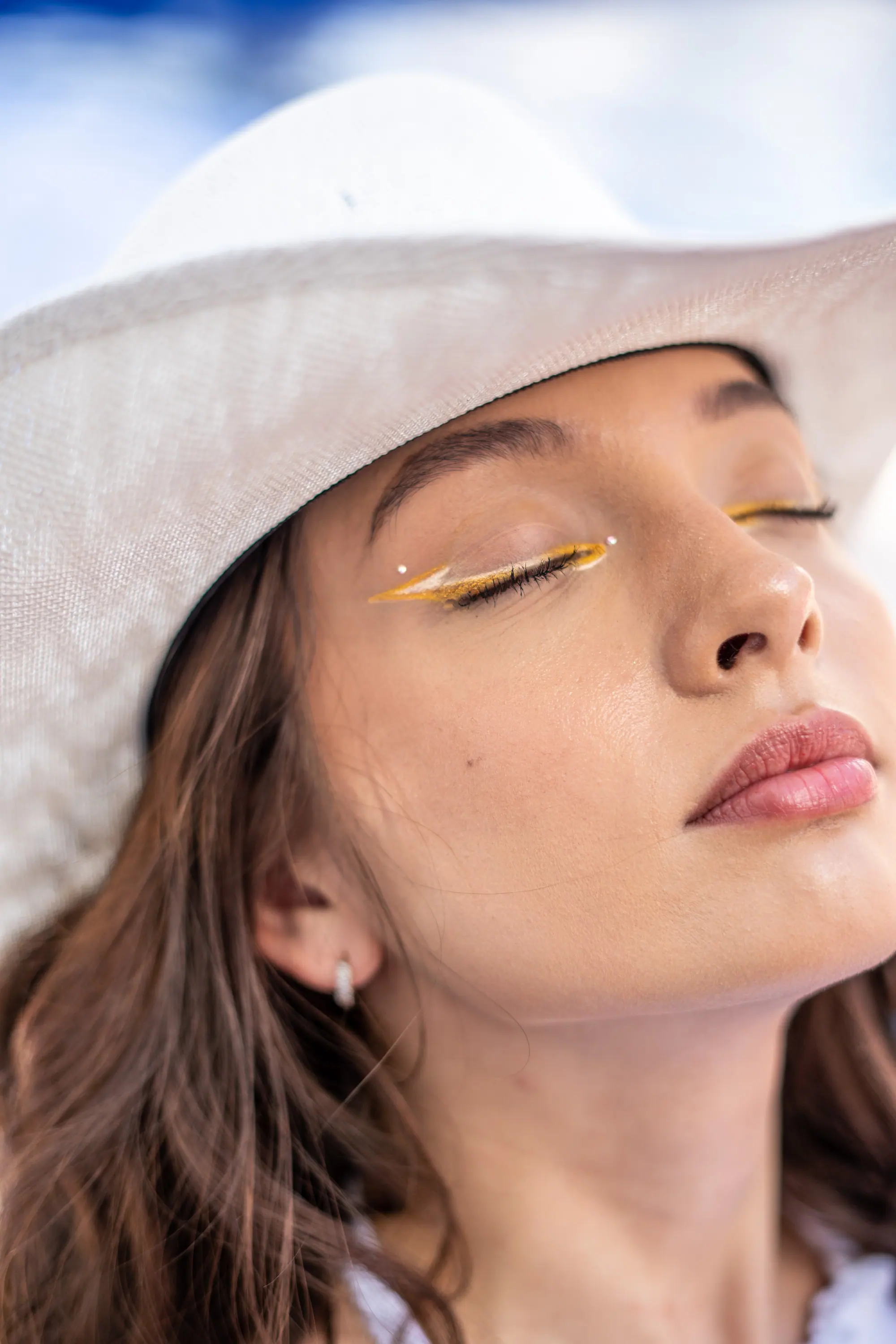 Rostro al sol con sombrero blanco y párpados dorados